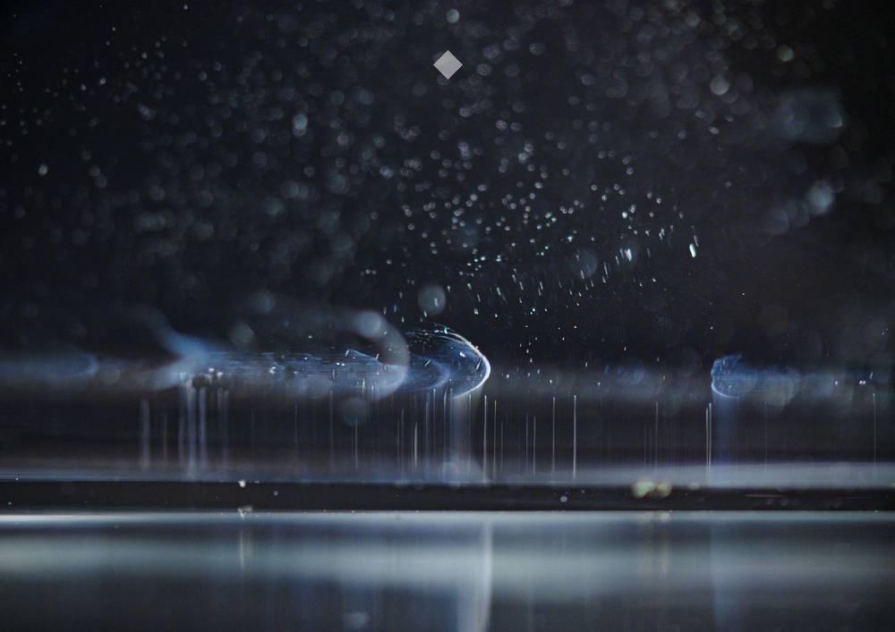 Jodie Luong, Untitled (5), 2026. Macro photograph of water droplets and spray, lit in cold blue against black.